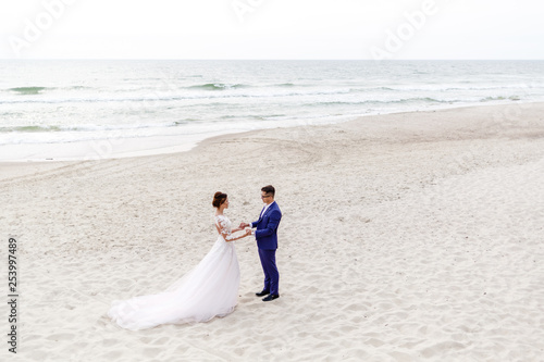 newlyweds walking along the sea beach at the wedding. The groom hugs the bride