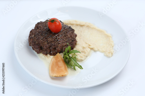 fried meat cutlet on a plate, with celery puree, garnished with tomato cherry and sour apples, isolated