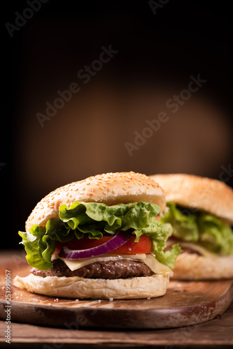 Tasty grilled beef burger with lettuce, cheese and onion served on cutting board with copyspace