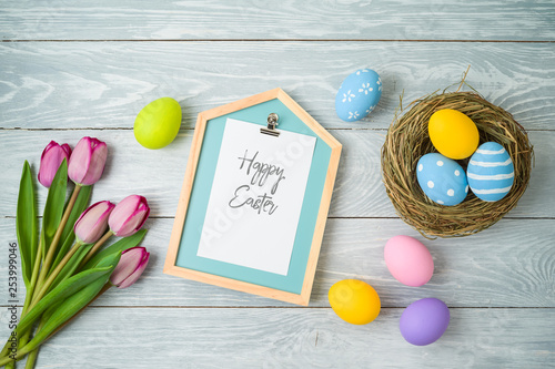 Photography Easter holiday background with easter eggs in bird nest, note and tulip flowers on wooden table