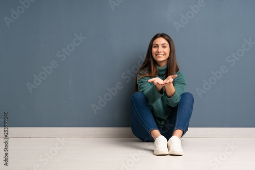 Young woman sitting on the floor holding copyspace imaginary on the palm to insert an ad
