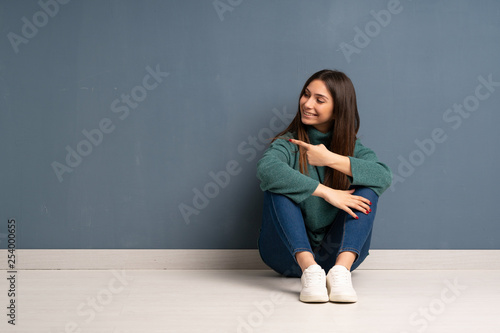 Young woman sitting on the floor pointing back