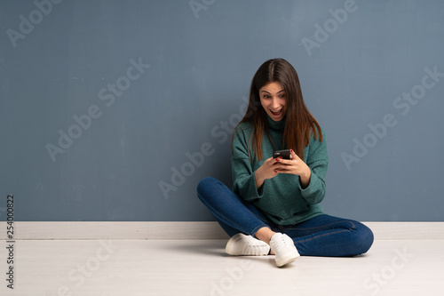 Young woman sitting on the floor surprised and sending a message