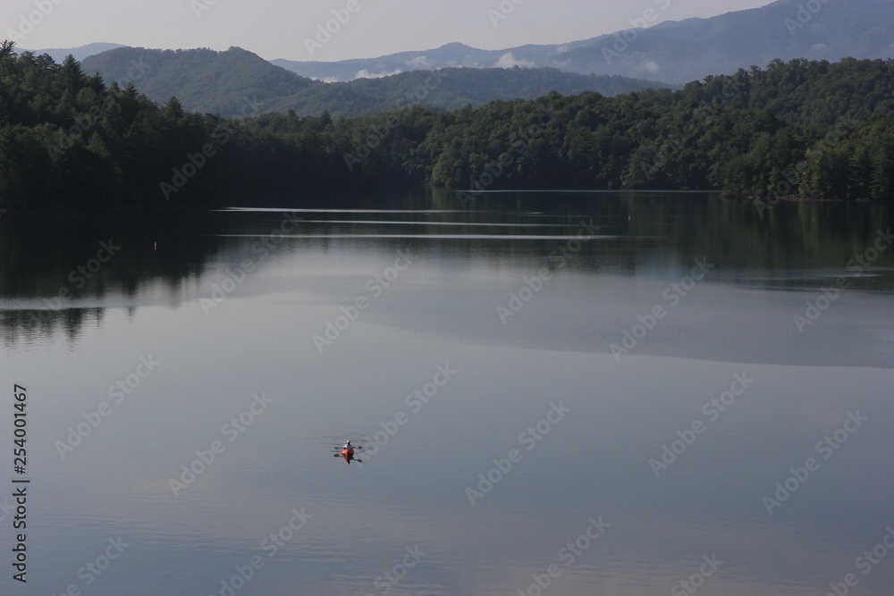 Active senior kayaking on a placid Lake Santeetlah, North Carolina, in wide angle view with mountains and woods in the background, Active senior kayaking on a placid Lake Santeetlah, North Carolina, in wide angle view with mountains and woods in the background,