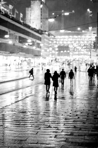 Silhouettes of people walking in rain in city street.