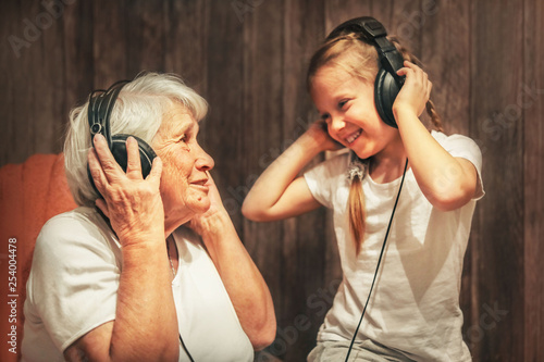 Obraz na plátně old woman and little girl in headphones listening to music grandmother and grand