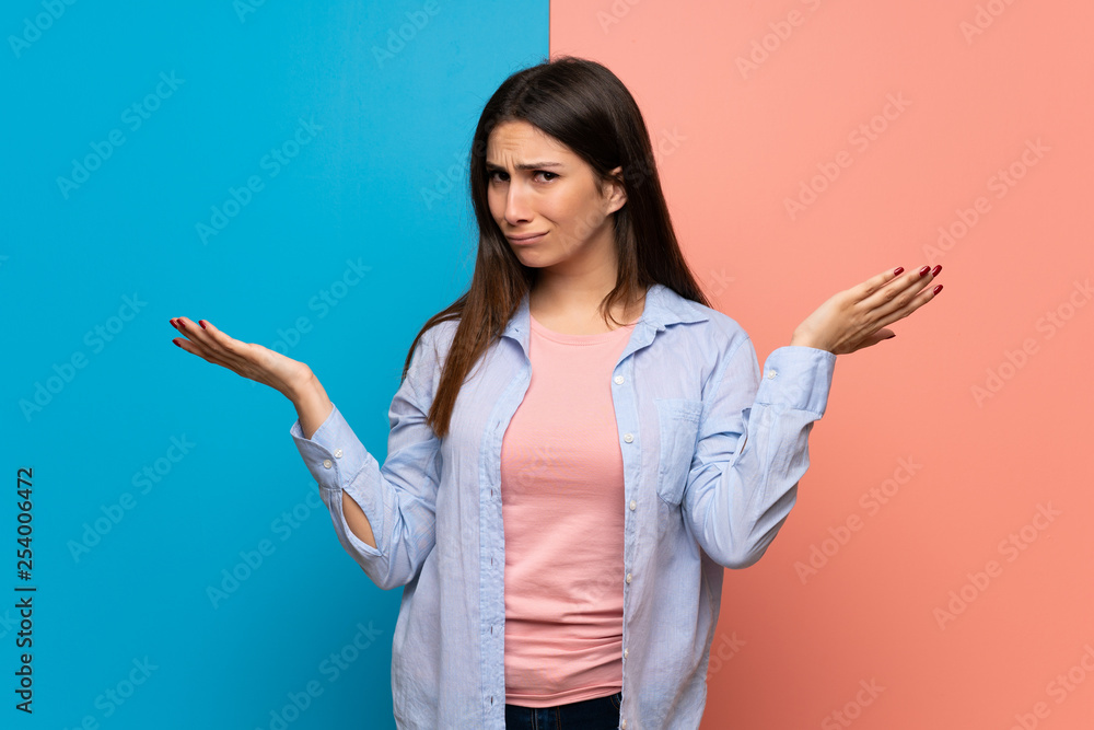 Young woman over pink and blue wall unhappy and frustrated with something because not understand something