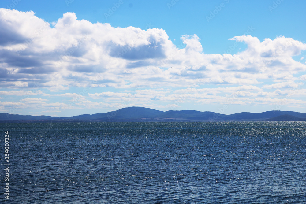 Beautiful seascape illuminated by the sun. Dark blue sea blue sky and white clouds. Mountains are visible on the horizon.