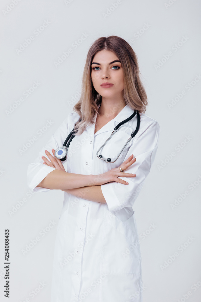 Medical physician doctor woman with crossed hands in white coat with stethoscope looks at camera on light background. Medical physician doctor woman with crossed hands in white coat with stethoscope looks at camera on light background.