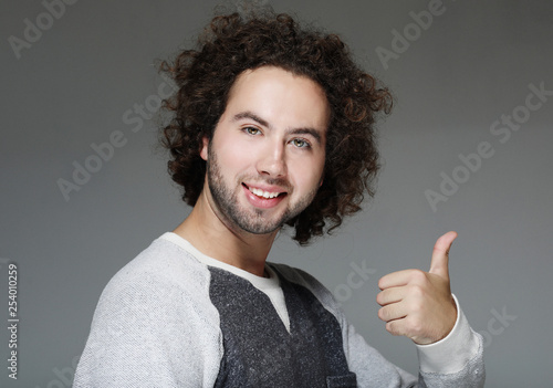 smiling curly man showing thumb up over gray background