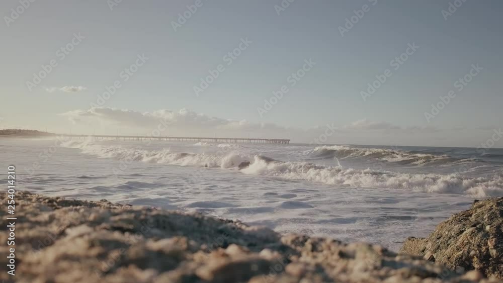 Close up slow motion sandy beach, rolling waves with view of Venice beach pier across the water in distance on sunny day. Close up slow motion sandy beach, rolling waves with view of Venice beach pier across the water in distance on sunny day.