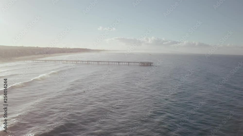 Slow aerial drone flight towards hazy sunrise view of Santa Monica pier over ocean waves heading towards Venice beach coastline. Slow aerial drone flight towards hazy sunrise view of Santa Monica pier over ocean waves heading towards Venice beach coastline.