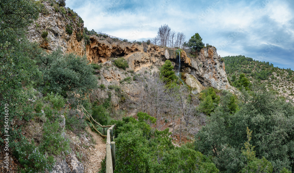 Track to caves and waterfall against cloudy sky Track to caves and waterfall against cloudy sky