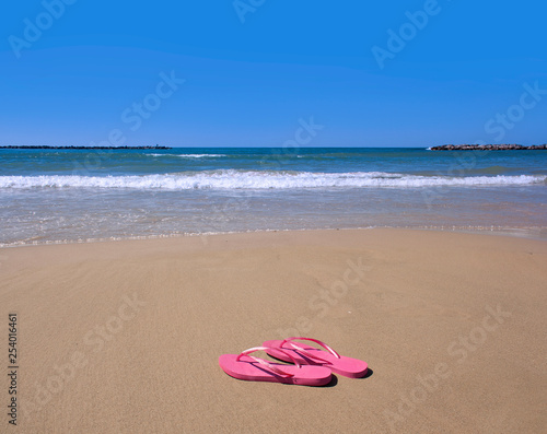 pink flip-flops on yellow sand at the water's edge on the beach