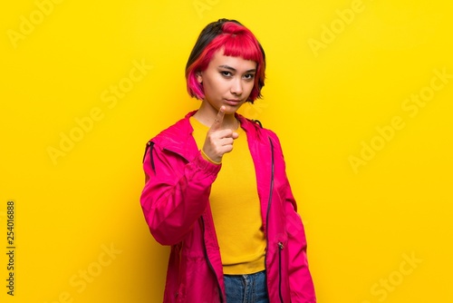 Young woman with pink hair over yellow wall frustrated and pointing to the front
