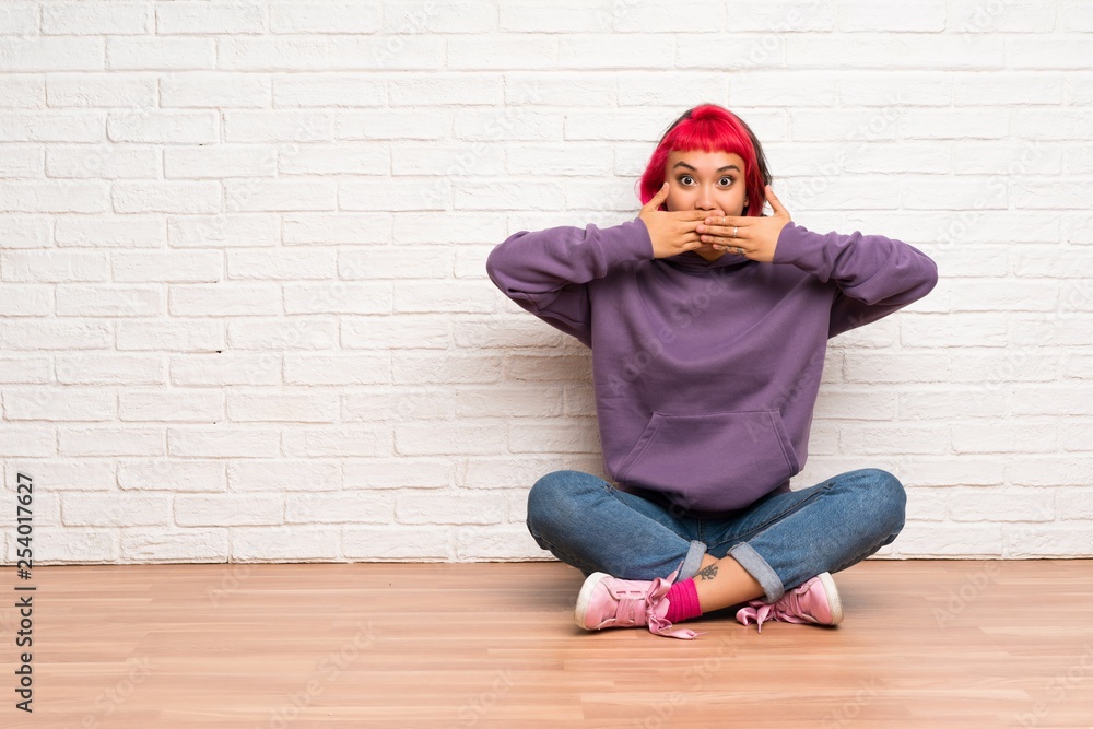 Young woman with pink hair sitting on the floor covering mouth with hands Young woman with pink hair sitting on the floor covering mouth with hands