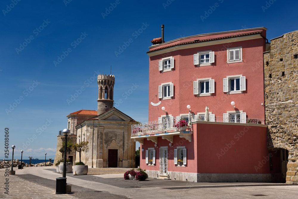 Naklejka premium Red stucco apartment on the Adriatic Sea coast at Piran Slovenia next to the Punta lighthouse and 13th century Church of St Clement