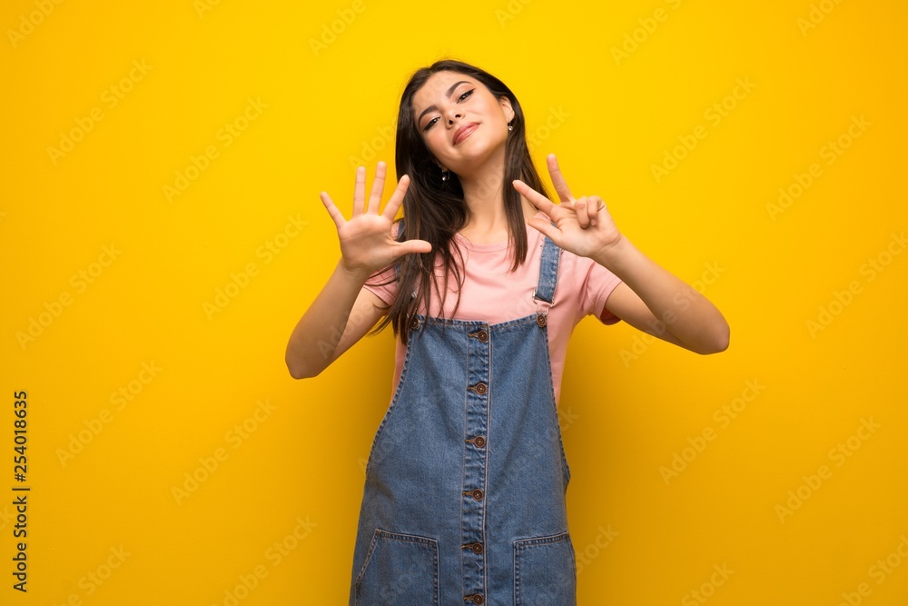 Teenager girl over yellow wall counting eight with fingers Teenager girl over yellow wall counting eight with fingers
