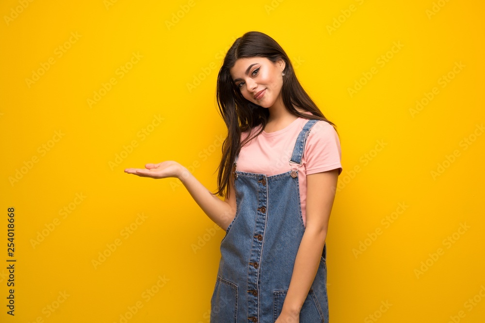 Teenager girl over yellow wall presenting an idea while looking smiling towards Teenager girl over yellow wall presenting an idea while looking smiling towards
