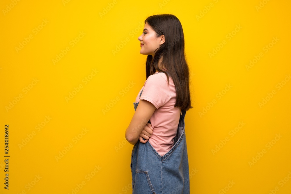 Teenager girl over yellow wall in lateral position Teenager girl over yellow wall in lateral position