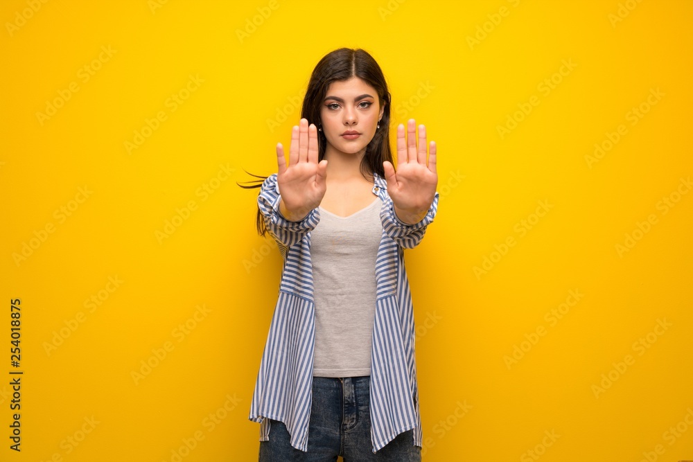 Teenager girl over yellow wall making stop gesture and disappointed Teenager girl over yellow wall making stop gesture and disappointed