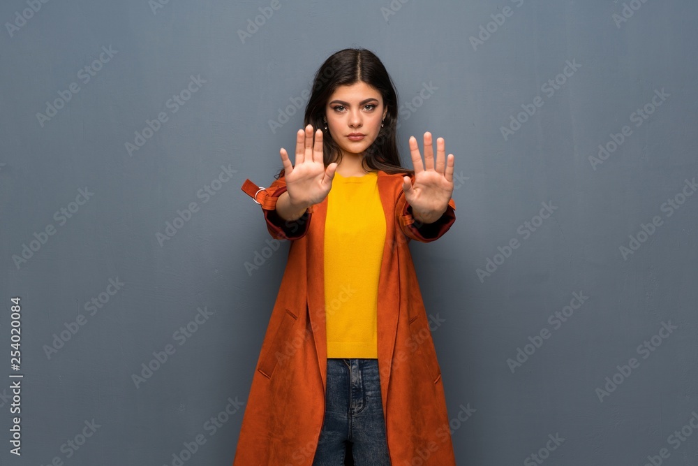 Teenager girl with coat over grey wall making stop gesture and disappointed Teenager girl with coat over grey wall making stop gesture and disappointed