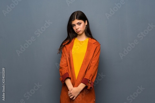 Teenager girl with coat over grey wall with sad and depressed expression © luismolinero