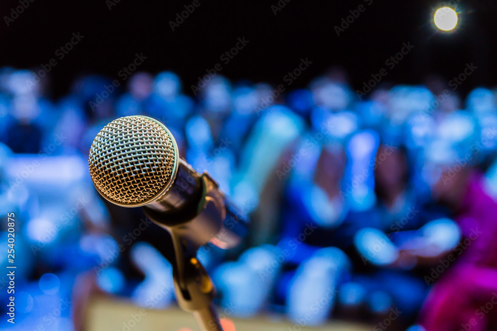 Wireless microphone on the stand. Blurred background. People in the audience. Show on stage in the theater or concert hall. Wireless microphone on the stand. Blurred background. People in the audience. Show on stage in the theater or concert hall.