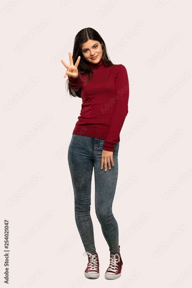 A full-length shot of a Teenager girl with turtleneck happy and counting three with fingers over isolated background A full-length shot of a Teenager girl with turtleneck happy and counting three with fingers over isolated background