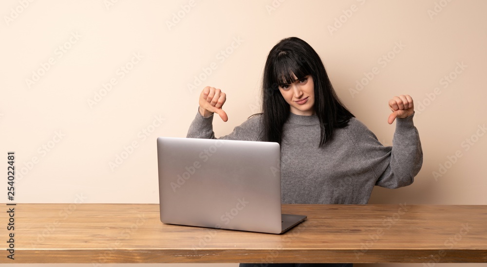 Young woman working with her laptop showing thumb down Young woman working with her laptop showing thumb down