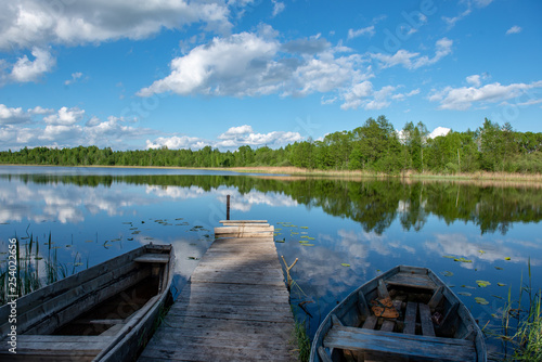 blue sky and cloud reflections in countryside lake in summer with boat and wooden boardwalk