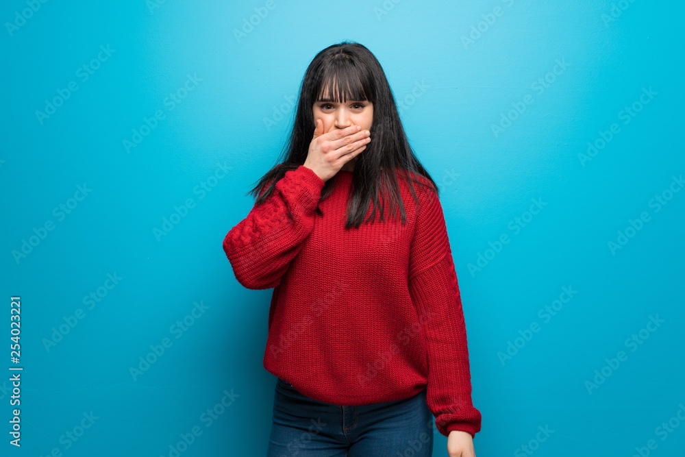 Woman with red sweater over blue wall covering mouth with hands for saying something inappropriate Woman with red sweater over blue wall covering mouth with hands for saying something inappropriate