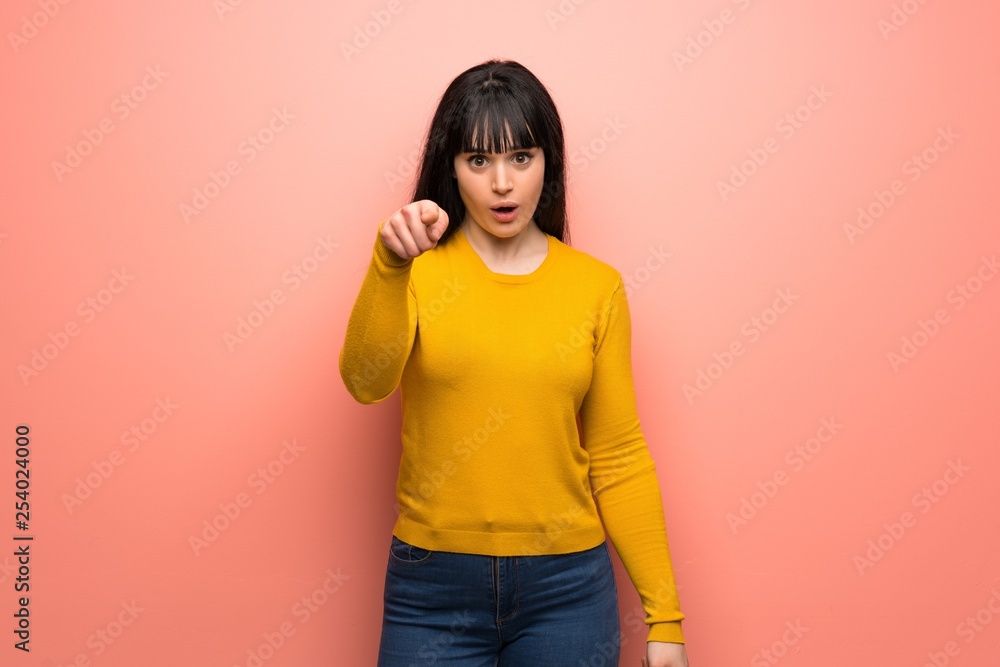Woman with yellow sweater over pink wall surprised and pointing front Woman with yellow sweater over pink wall surprised and pointing front