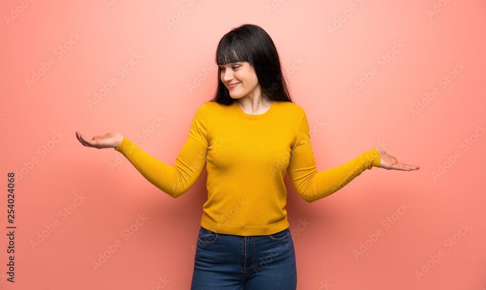Woman with yellow sweater over pink wall holding copyspace with two hands Woman with yellow sweater over pink wall holding copyspace with two hands