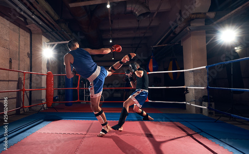 Two sportsmen kickboxers exercising kickboxing in the ring at the sport club