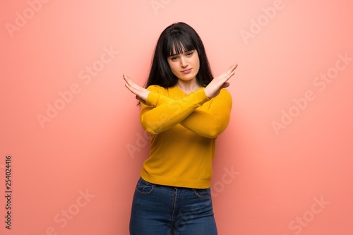 Woman with yellow sweater over pink wall making NO gesture