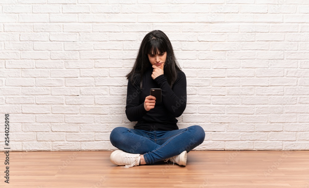 Woman sitting on the floor thinking and sending a message Woman sitting on the floor thinking and sending a message
