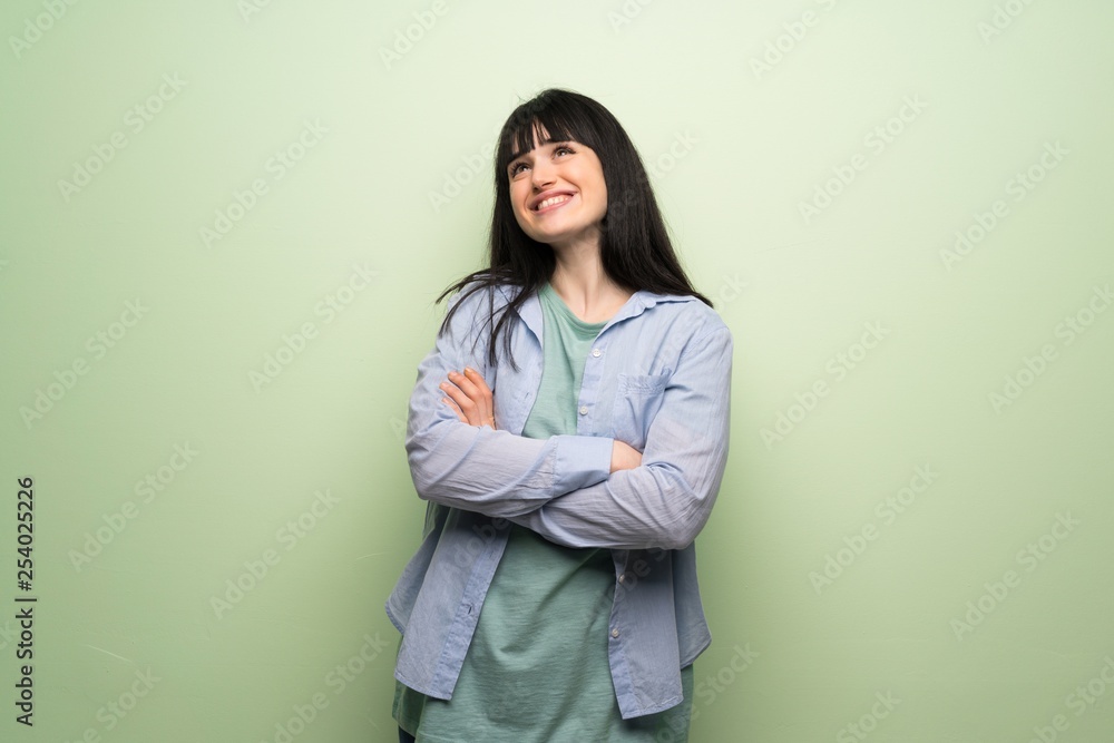 Young woman over green wall looking up while smiling Young woman over green wall looking up while smiling