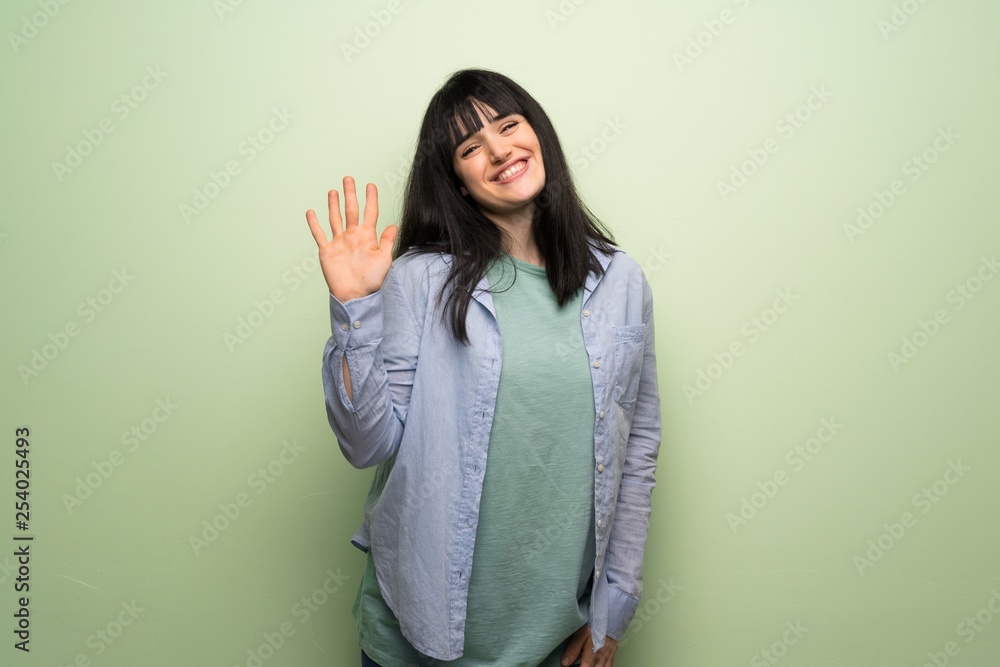 Young woman over green wall saluting with hand with happy expression Young woman over green wall saluting with hand with happy expression