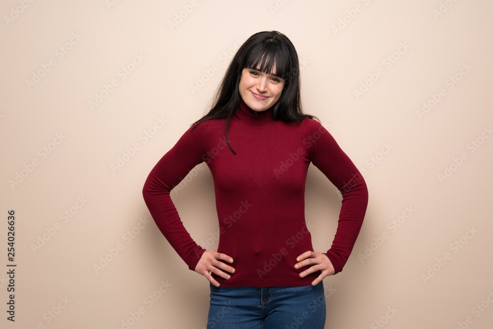 Young woman with red turtleneck posing with arms at hip and laughing looking to the front Young woman with red turtleneck posing with arms at hip and laughing looking to the front
