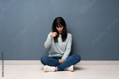 Woman sitting on the floor surprised and pointing front
