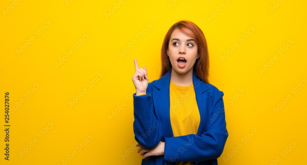 Young redhead woman with trench coat thinking an idea pointing the finger up Young redhead woman with trench coat thinking an idea pointing the finger up