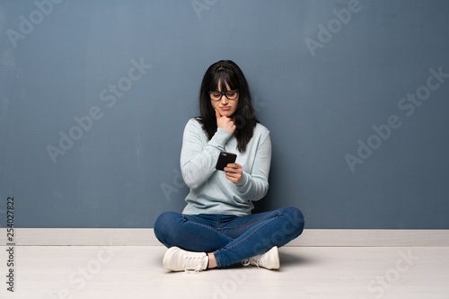 Woman sitting on the floor thinking and sending a message