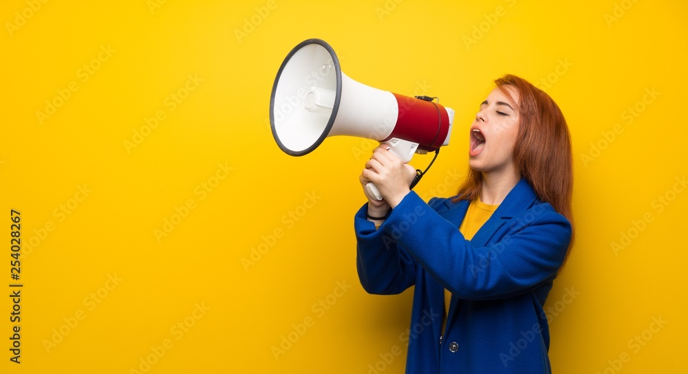 Young redhead woman with trench coat shouting through a megaphone Young redhead woman with trench coat shouting through a megaphone