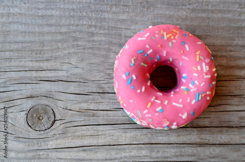 Donut with pink icing on wooden background with space for text. Flat lay. Food concept.Minimalism.Top view. 