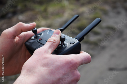 Remote controller in male hands close-up. Man holding transmitter and piloting some vehicle. Drone, rc car or helicopter running. Leisure, hobby, entertainment concept.