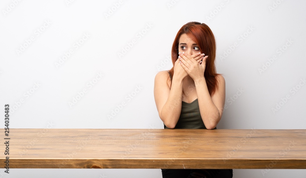Young redhead woman at desk covering mouth and looking to the side Young redhead woman at desk covering mouth and looking to the side