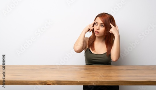 Young redhead woman at desk having doubts and thinking