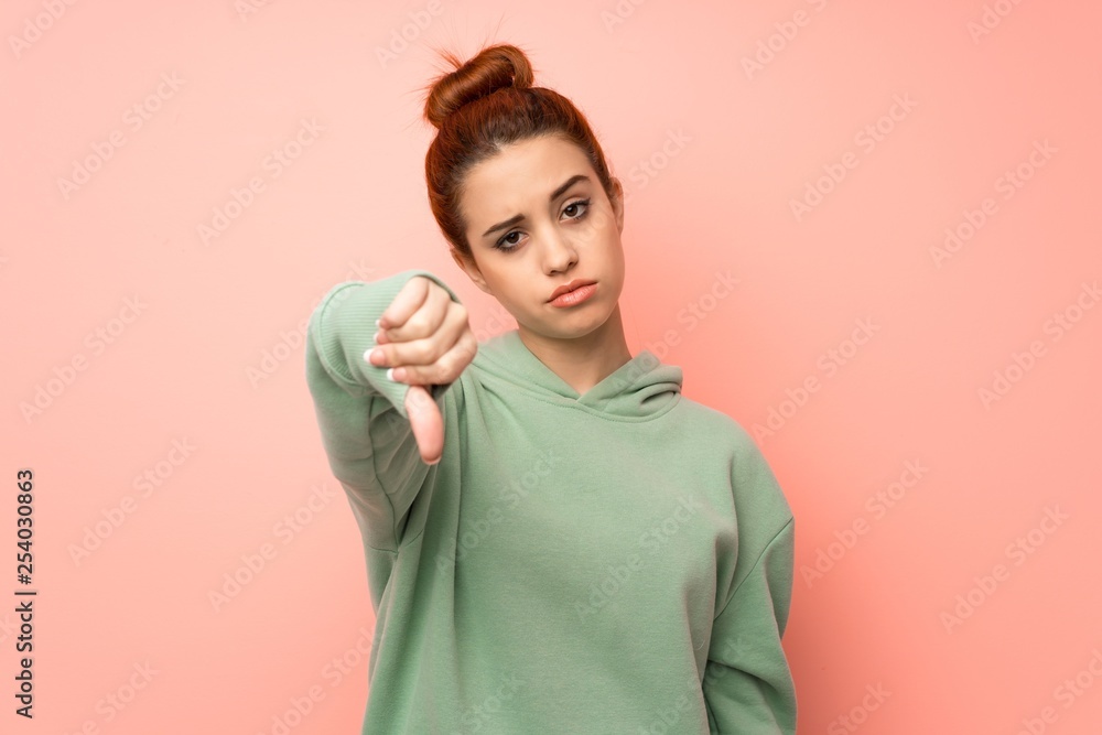 Fototapeta premium Young redhead woman with sweatshirt showing thumb down with negative expression