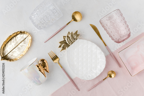 Flat lay of table decor. Top view of decorations for a serving festive table. White and golden pineapple plate, water glasses and pink cutlery on white background, flatlay. photo